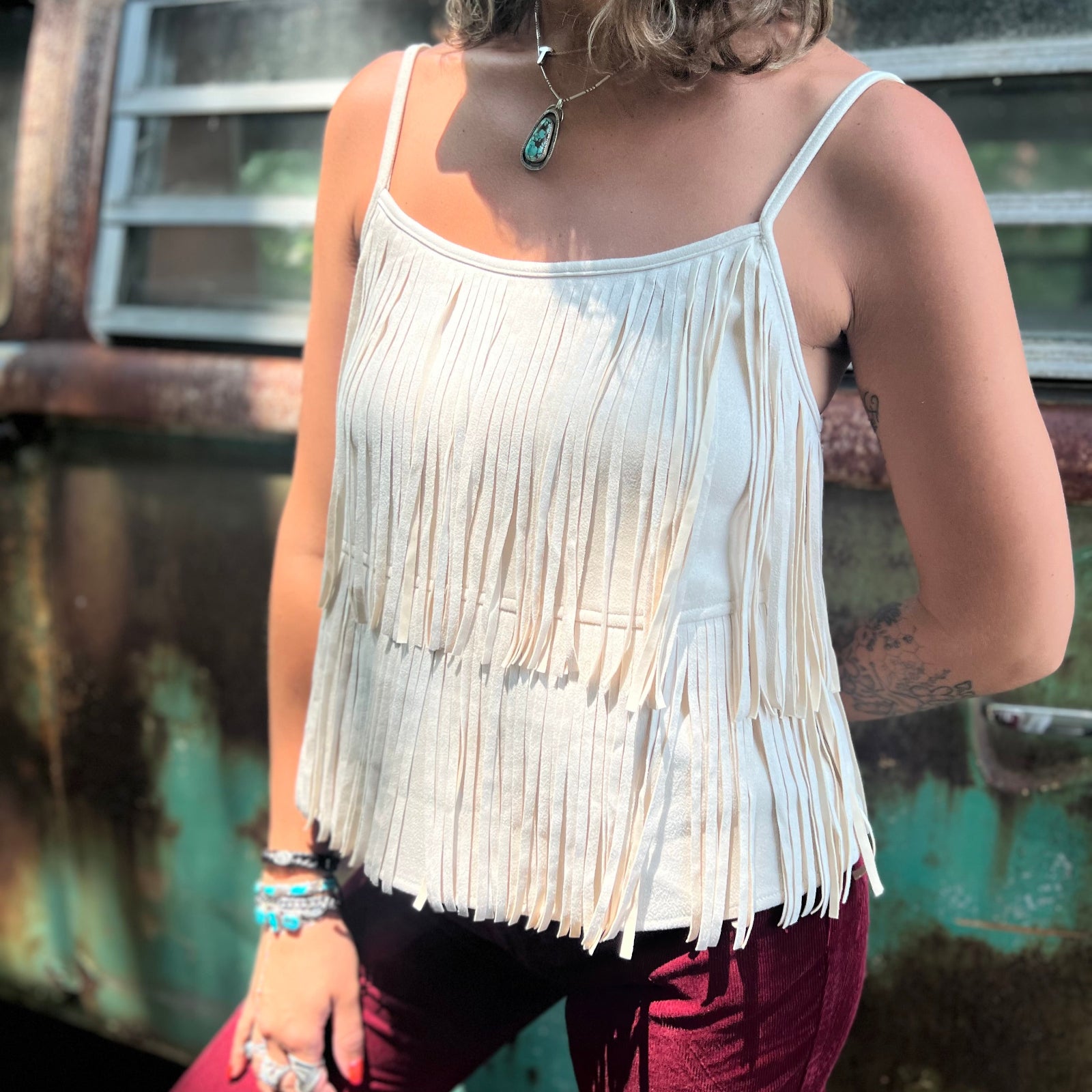 A woman wearing the Cream Fringe Faux Suede Cami with wine bell bottoms.