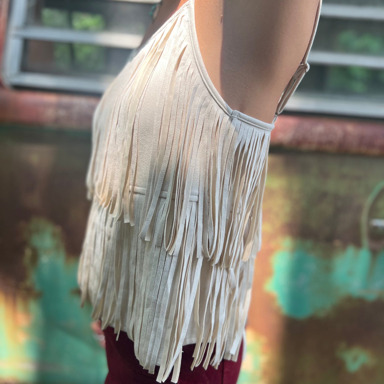 A woman wearing the Cream Fringe Faux Suede Cami with wine bell bottoms.