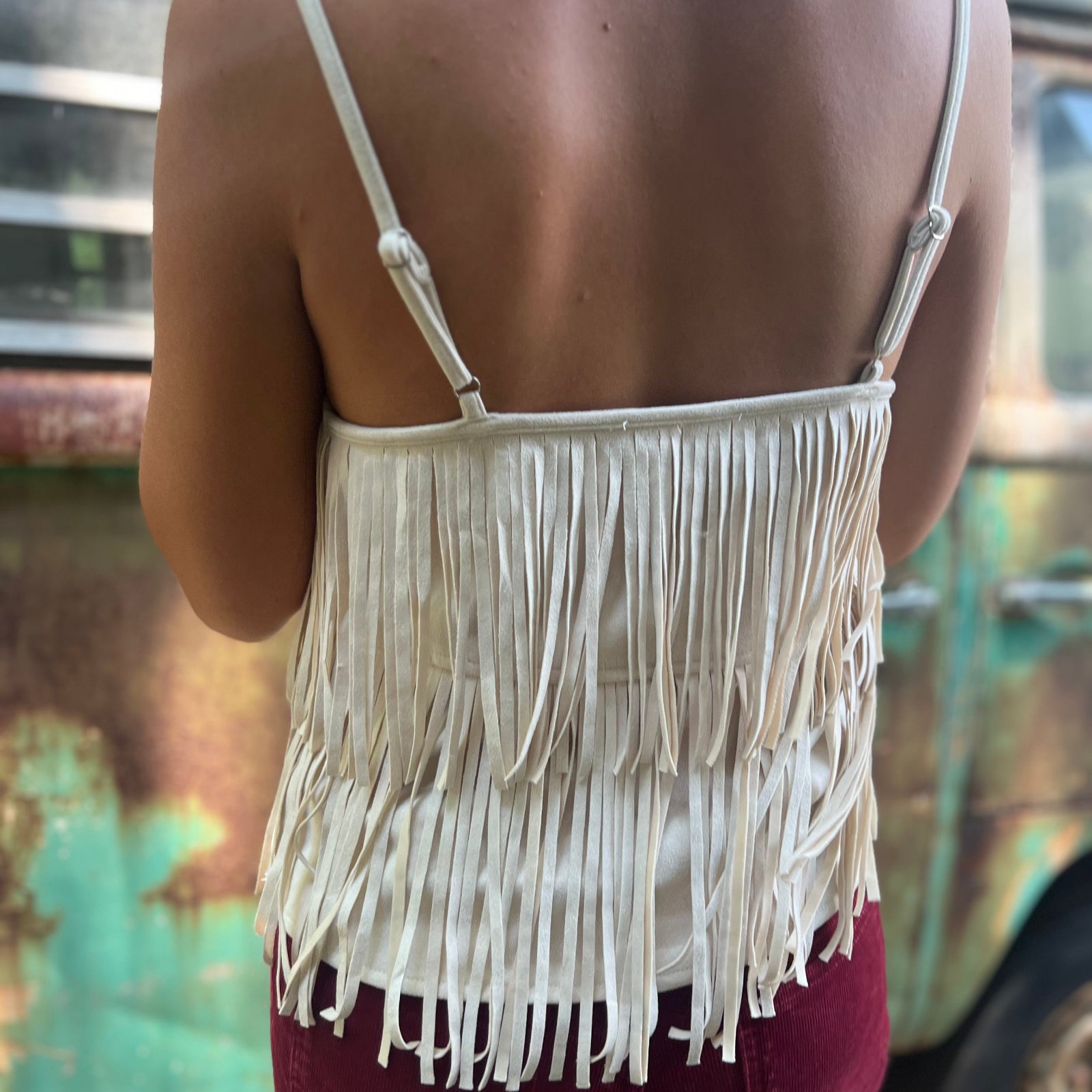 A woman wearing the Cream Fringe Faux Suede Cami with wine bell bottoms.