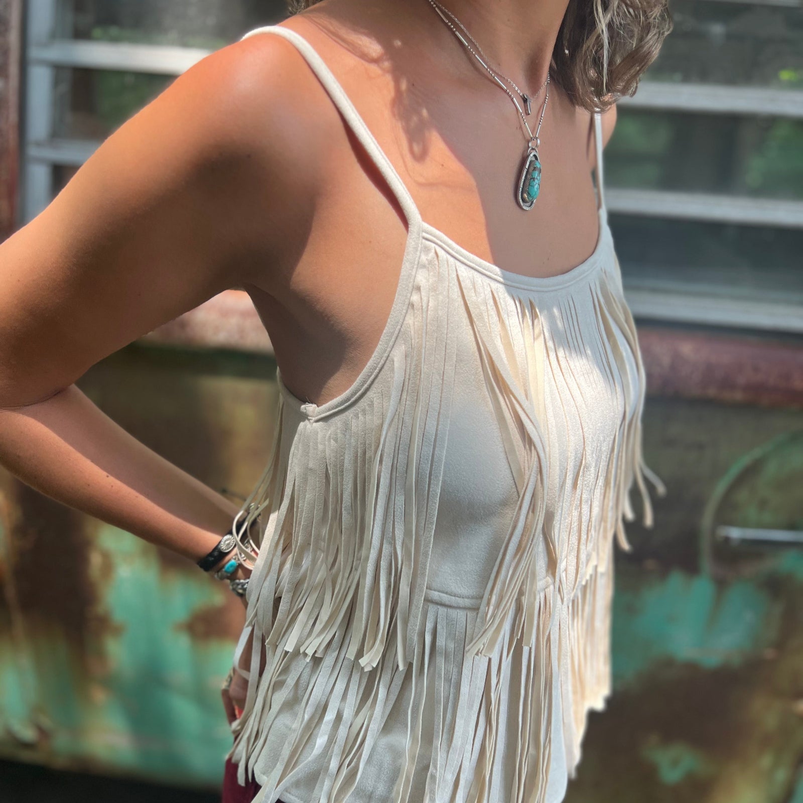 A woman wearing the Cream Fringe Faux Suede Cami with wine bell bottoms.