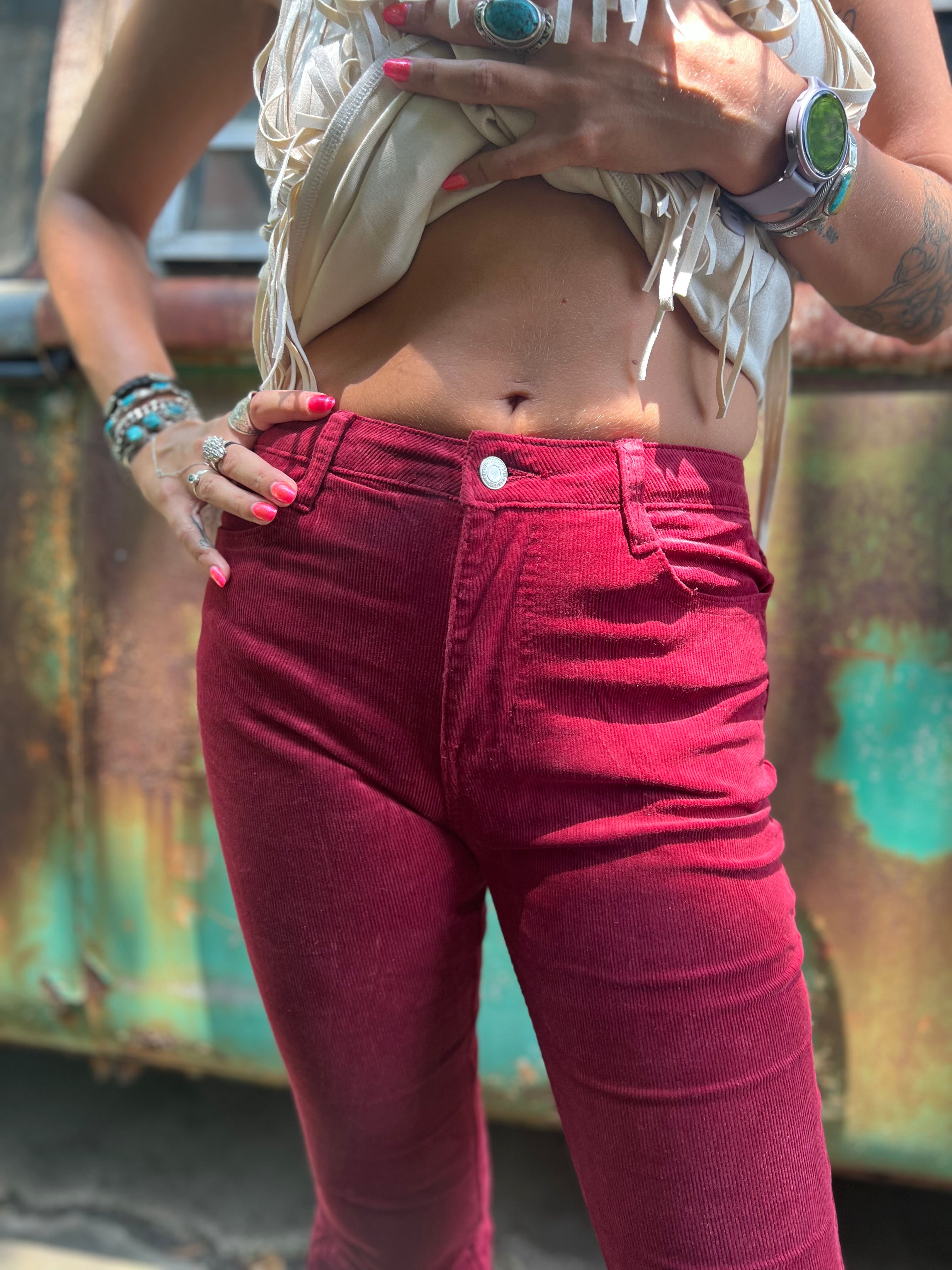 Someone wearing the Wine Soft Corduroy Flared Pants with Distressed Hem and a cream fringe top.