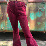 Someone wearing the Wine Soft Corduroy Flared Pants with Distressed Hem and a cream fringe top.