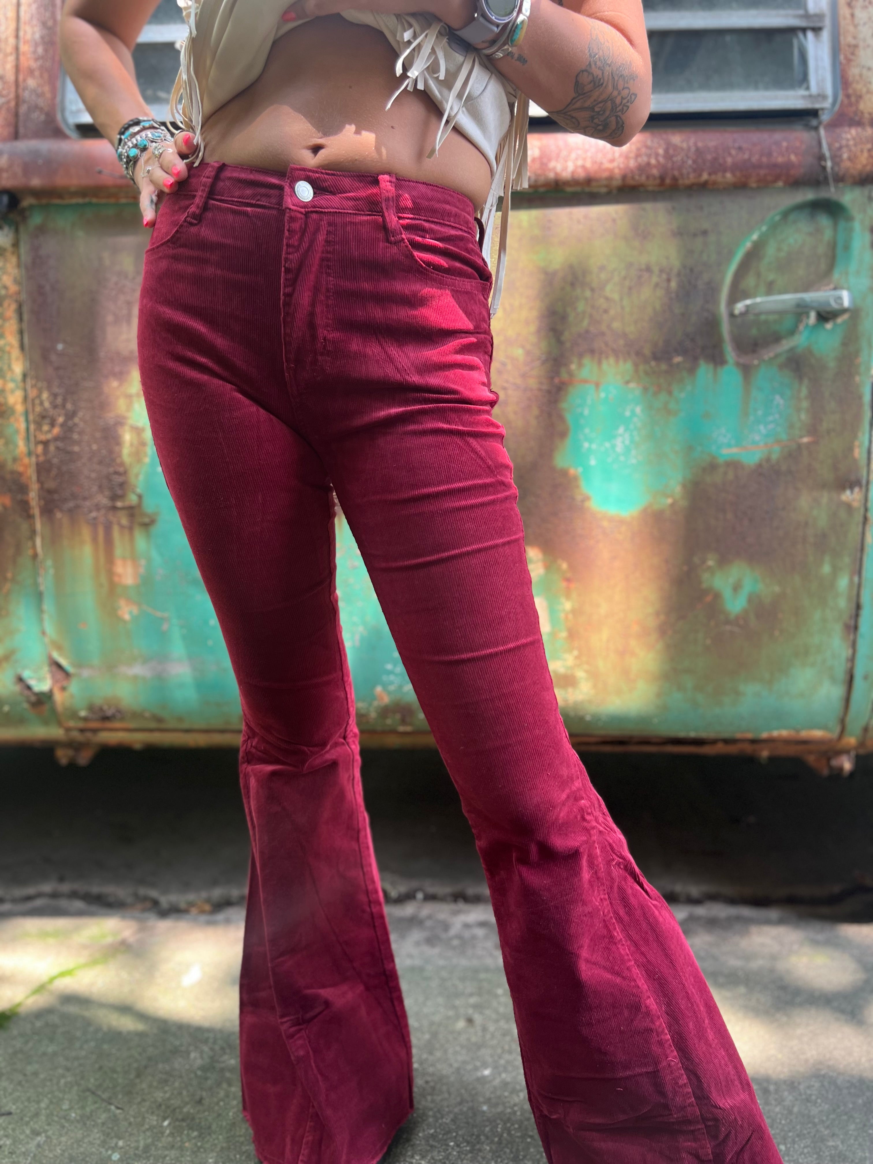 Someone wearing the Wine Soft Corduroy Flared Pants with Distressed Hem and a cream fringe top.