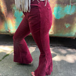 Someone wearing the Wine Soft Corduroy Flared Pants with Distressed Hem and a cream fringe top.