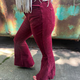 Someone wearing the Wine Soft Corduroy Flared Pants with Distressed Hem and a cream fringe top.