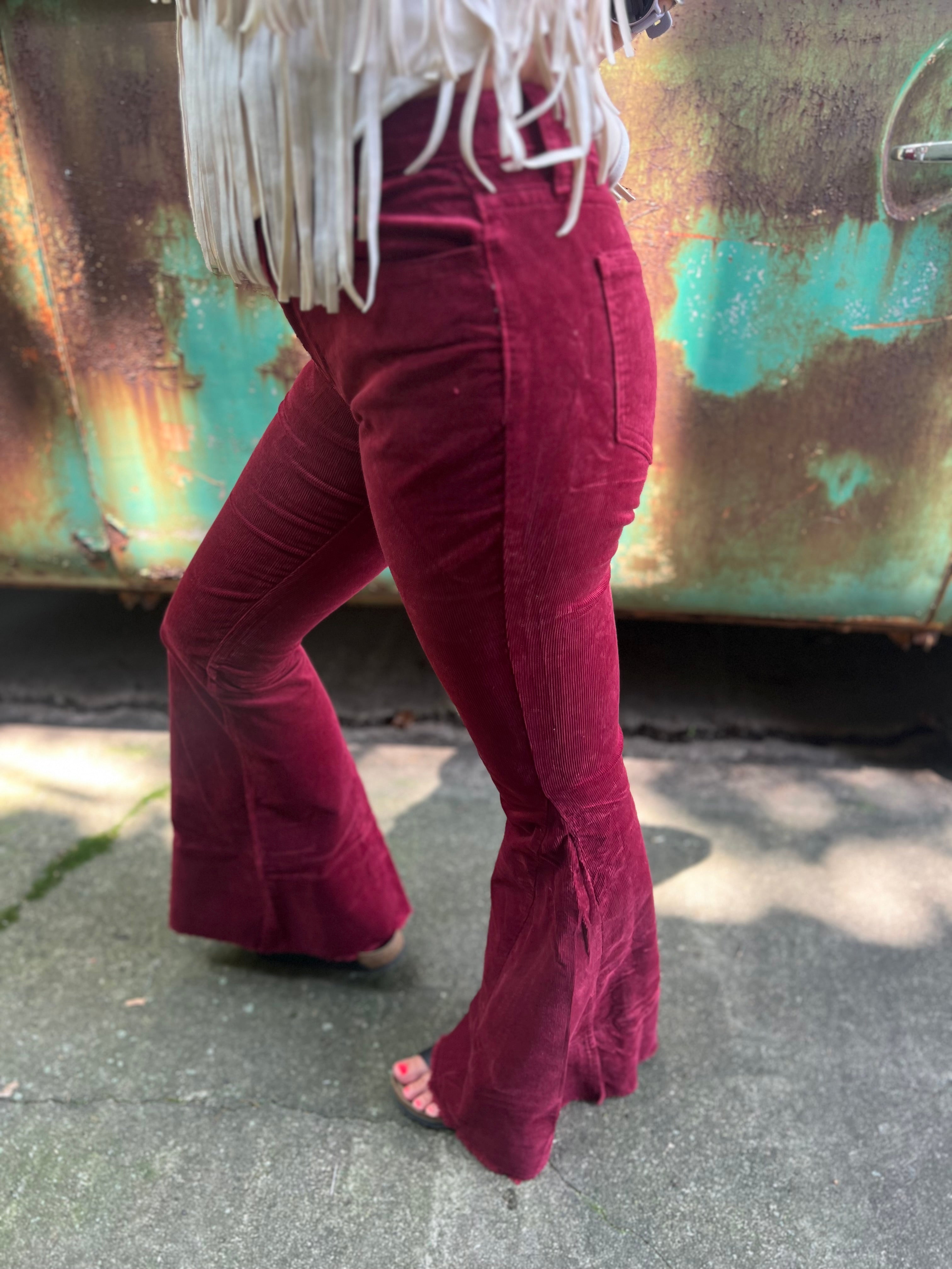 Someone wearing the Wine Soft Corduroy Flared Pants with Distressed Hem and a cream fringe top.