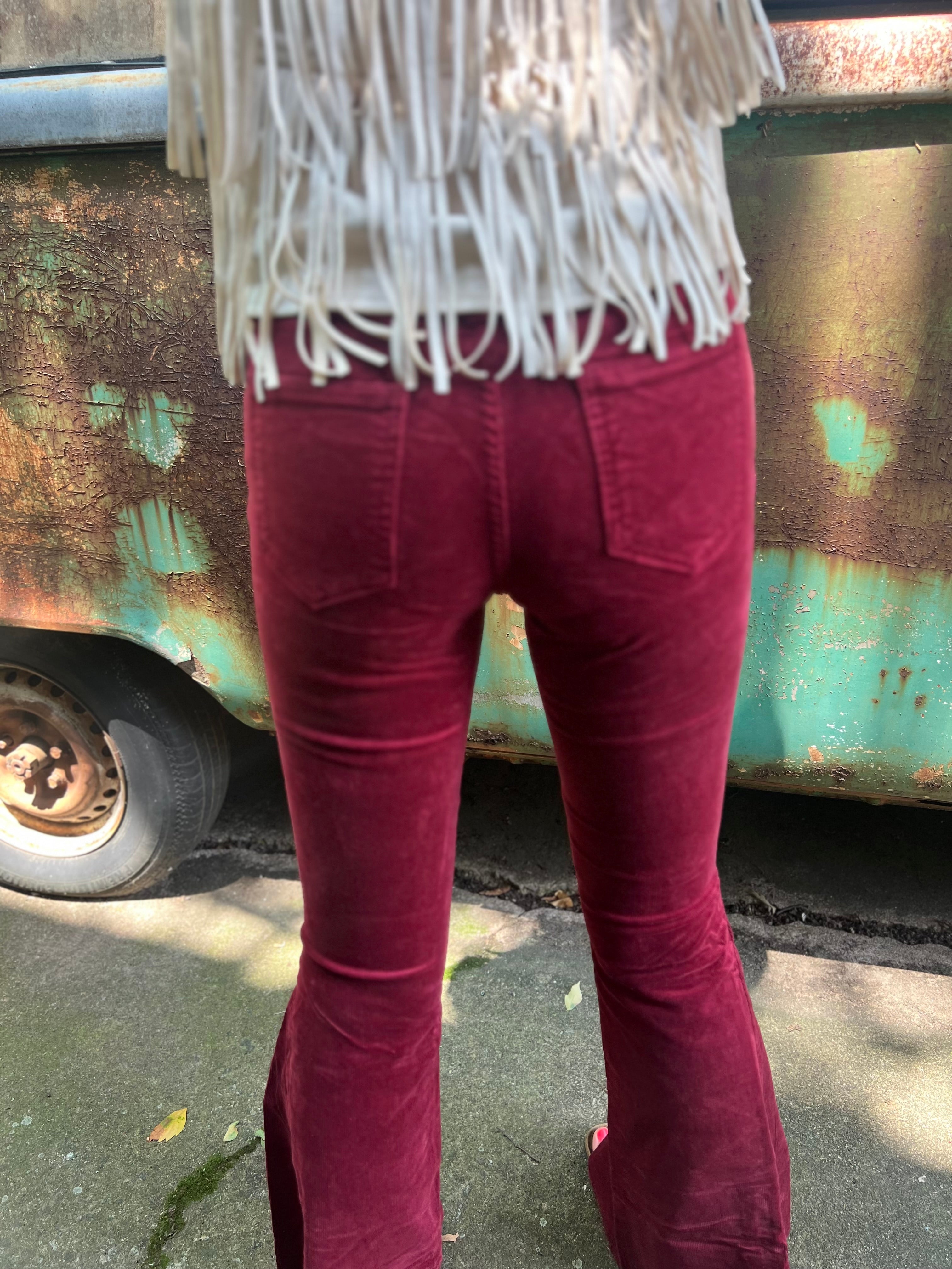 Someone wearing the Wine Soft Corduroy Flared Pants with Distressed Hem and a cream fringe top.