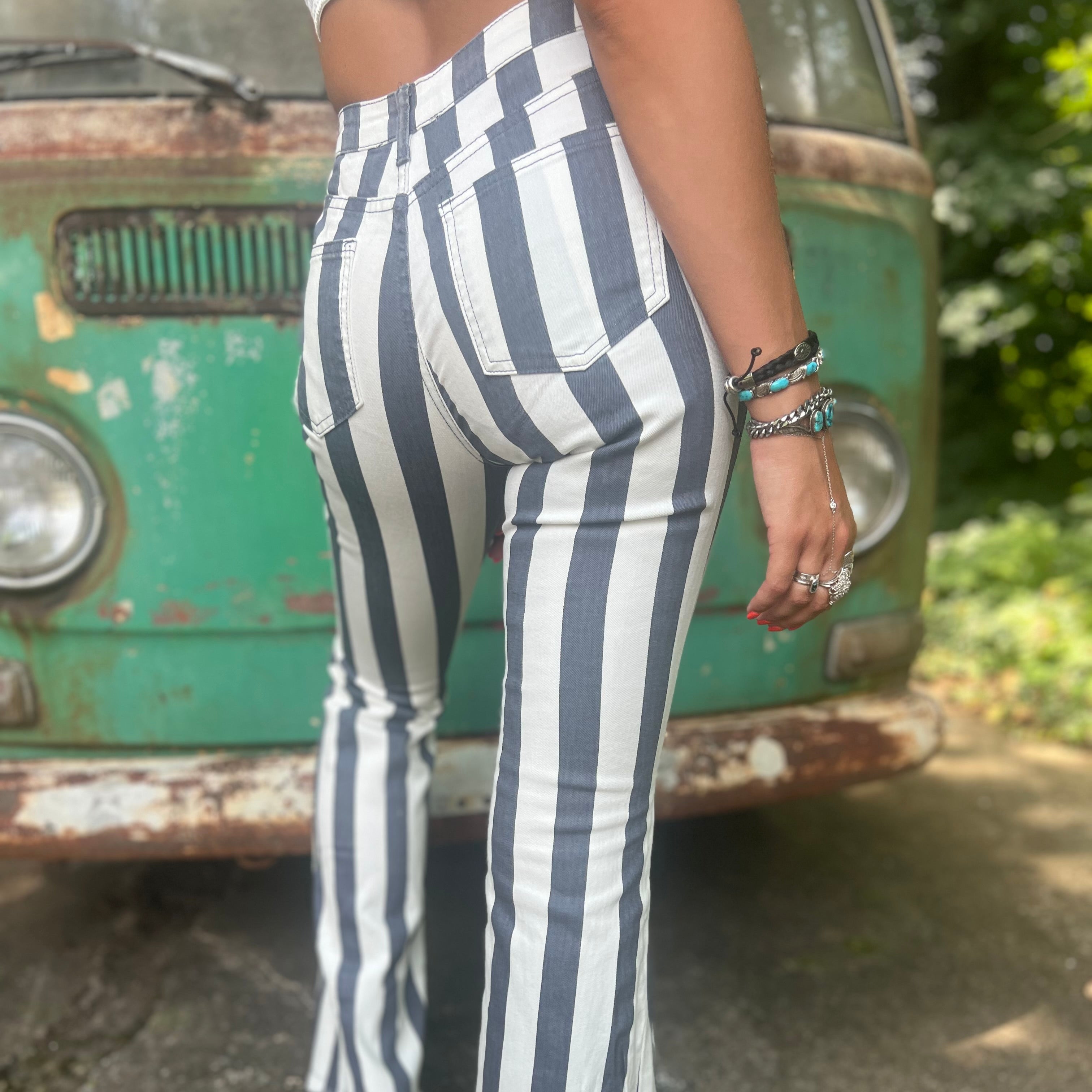 A woman wearing the Cream and Grey Striped Distressed Denim Bell Bottoms and a white bralette.