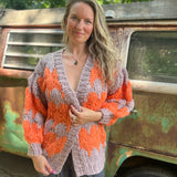 A woman wearing the Chunky Cardigan - Orange Taupe: One Size with a cream top and grey pants.
