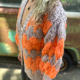 A woman wearing the Chunky Cardigan - Orange Taupe: One Size with a cream top and grey pants.