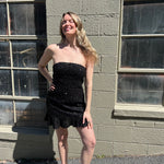 A woman wearing the black Sequin Lace-Up Back Strapless Mini Dress.