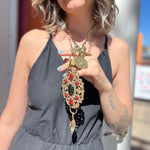 A woman wearing the Gypsy Junk Luxe-A 24" Length Necklace with a black dress with her hand underneath necklace lifting it up slightly.