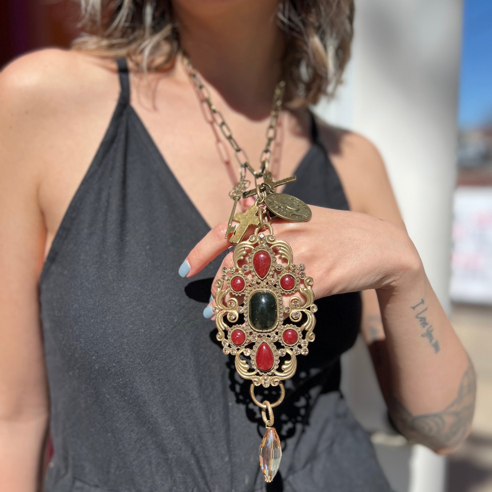 A woman wearing the Gypsy Junk Luxe-A 24" Length Necklace with a black dress with her hand underneath necklace lifting it up slightly.