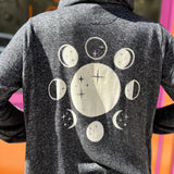 A woman wearing the black Moon Cycle Waterfall Hoodie with a black tank and bellbottoms in front of an orange and pink wall.