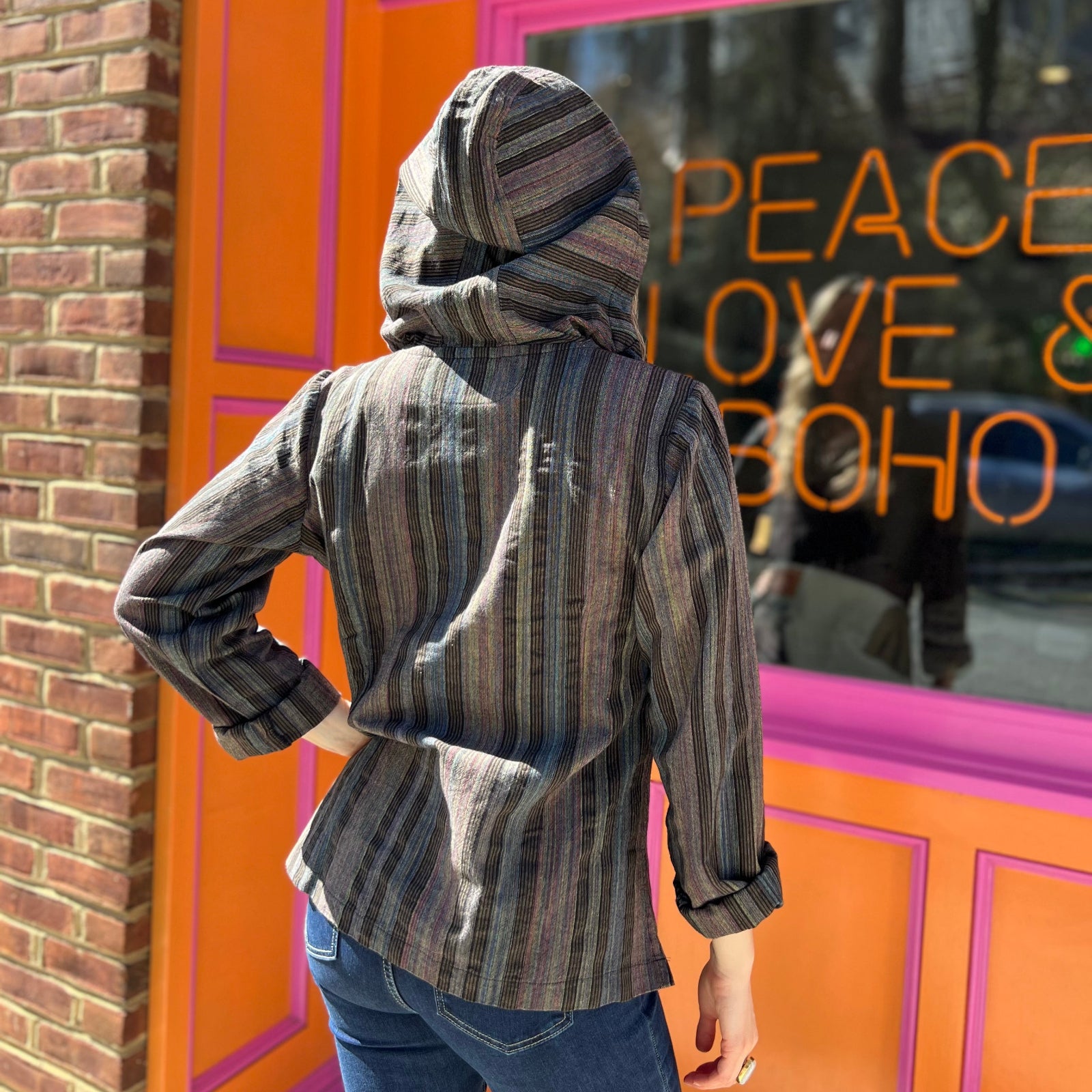 A woman wearing the agate Womens Half Button Baja Hoodie with jeans in front of a pink and orange wall.