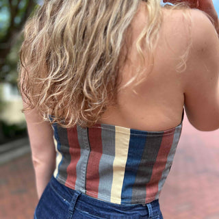 Rear view of woman walking in striped retro crop top and high-waisted flared jeans with wavy hair and hat