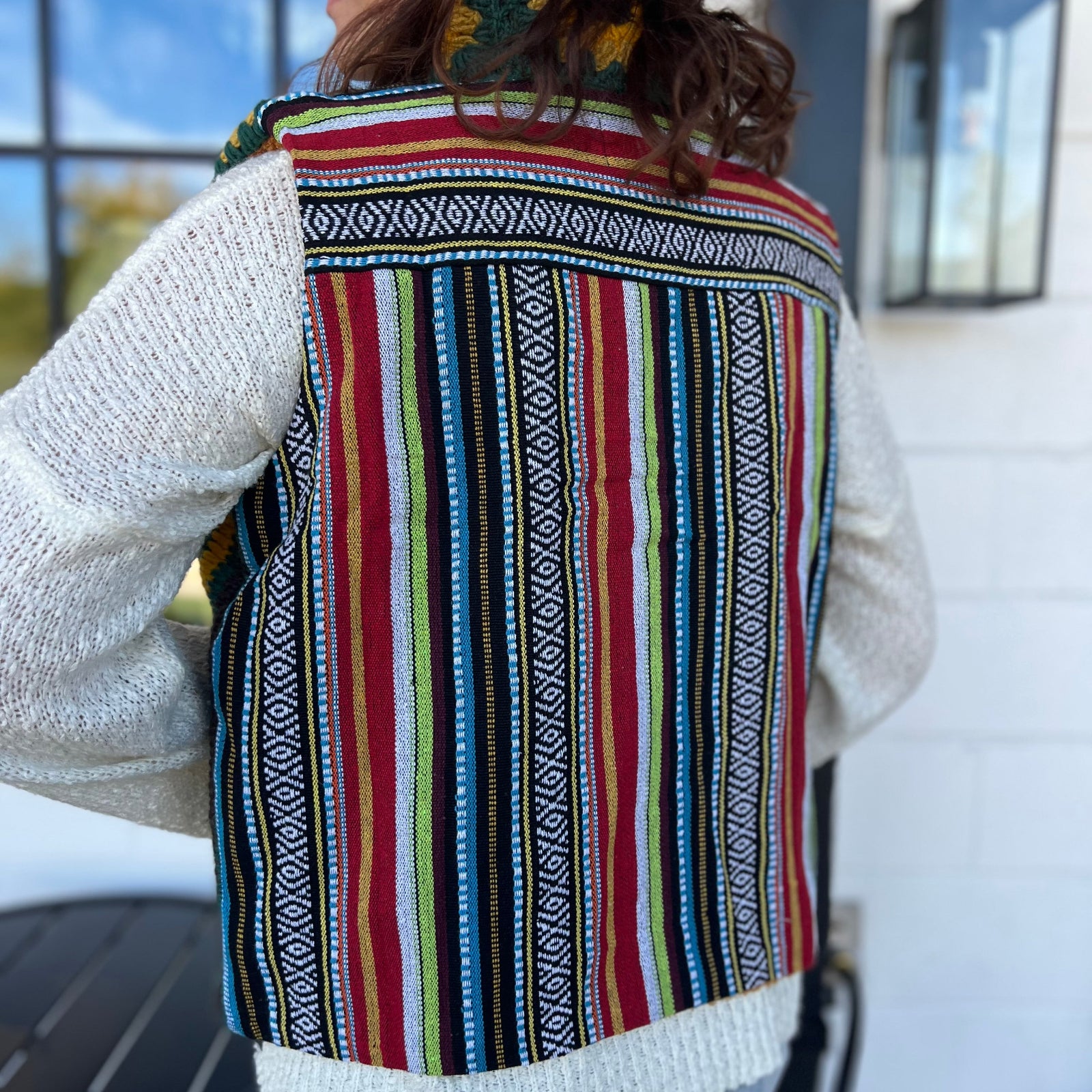 A woman wearing the Sunflower Flower Granny Square Fleece Lined Wool Vest with a white sweater and jeans, showing off the back.