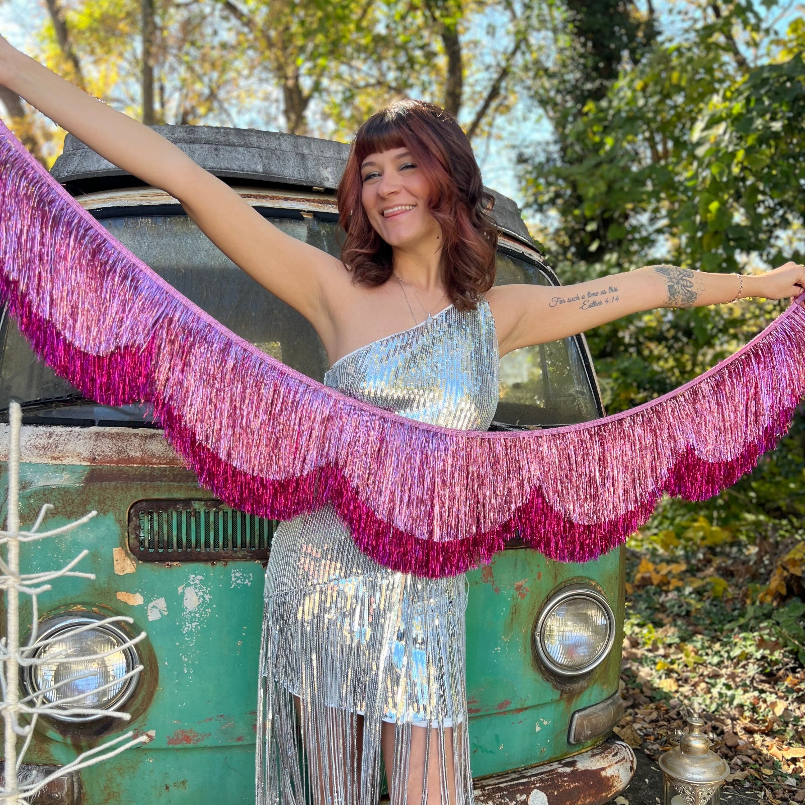 A woman holding the Tickled Pink Scalloped Layered Fringe Banner in front of a vintage teal Volkswagen bus.
