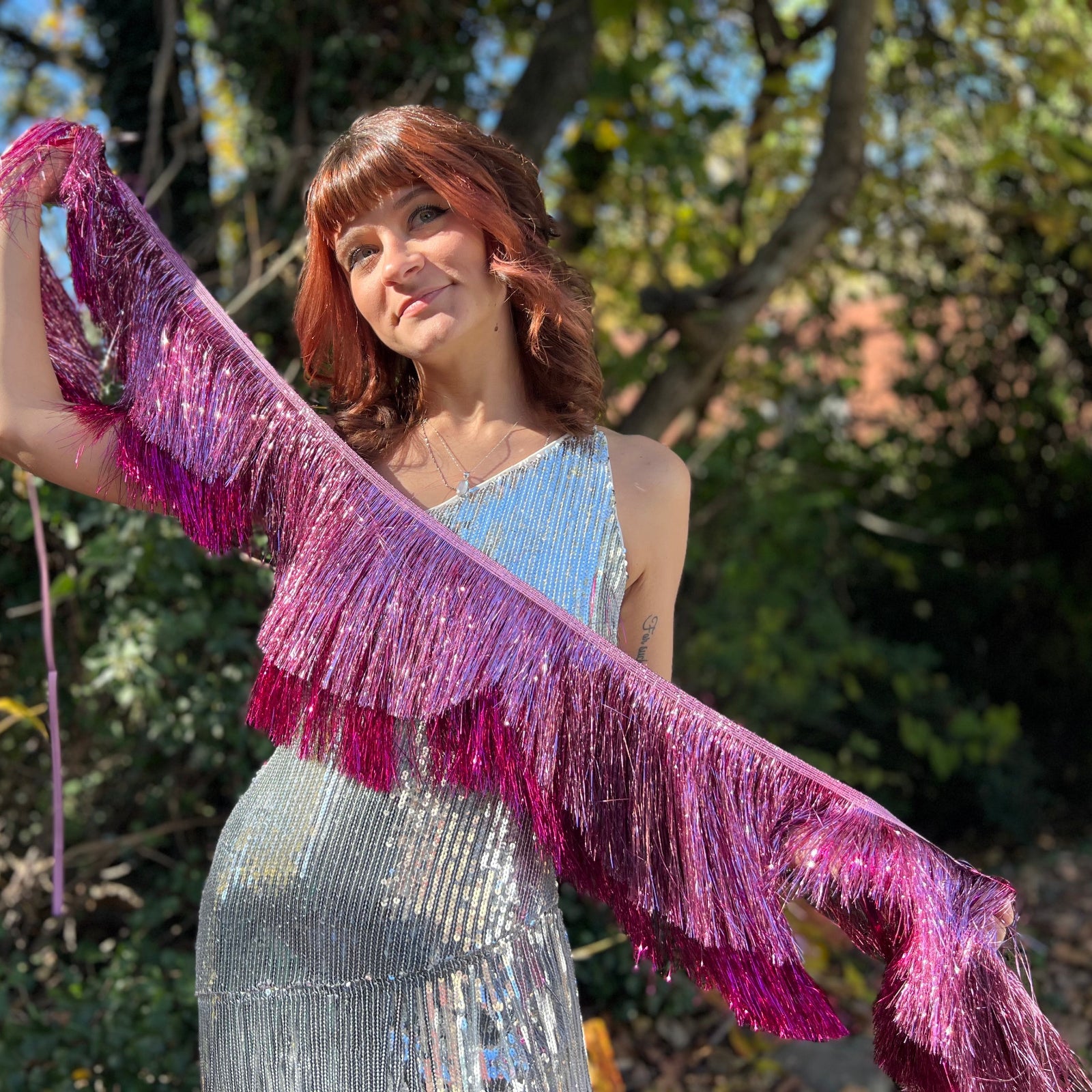 A woman holding the Tickled Pink Scalloped Layered Fringe Banner in front of trees.