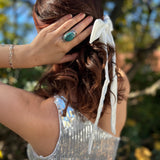 A woman wearing the Bride To Be Embroidered White Satin Bow with a silver sequin dress, showing off the side.