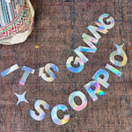 The It's Giving Scorpio Banner Iridescent Foil Banner on a rug.