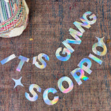 The It's Giving Scorpio Banner Iridescent Foil Banner on a rug.