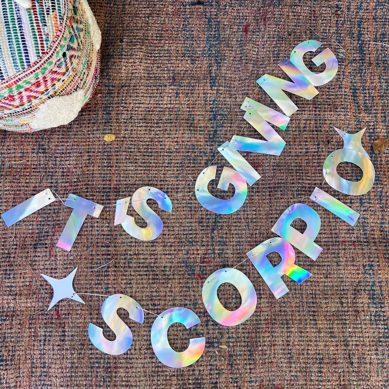 The It's Giving Scorpio Banner Iridescent Foil Banner on a rug.