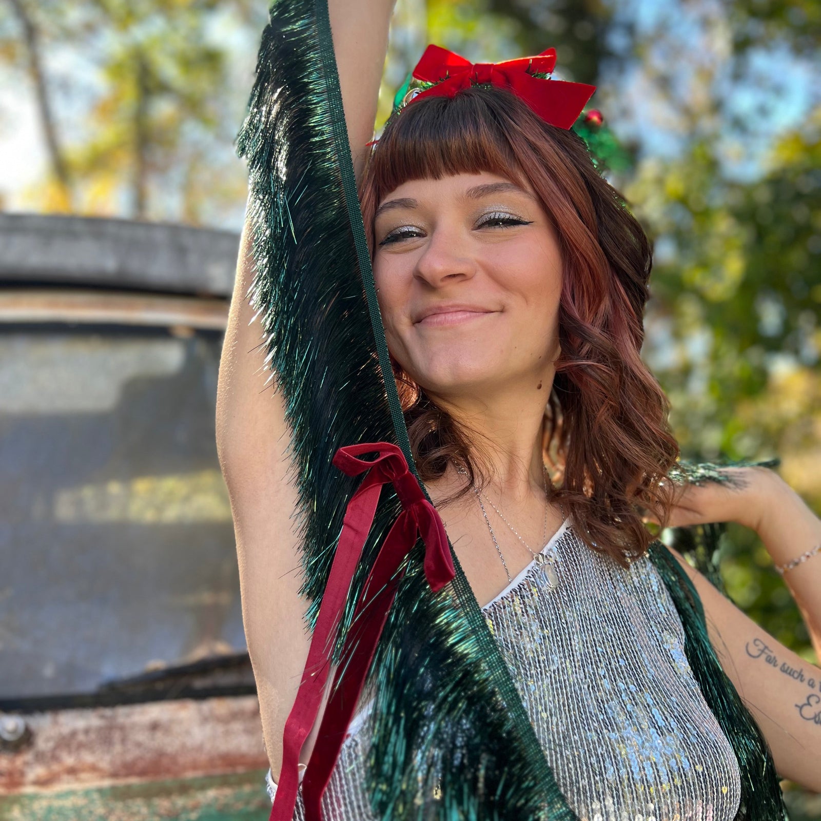 A woman in a silver sequin dress holding the Xmas Velvet Bow & Green Fringe Banner in front of a vintage teal Volkswagen bus.