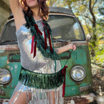 A woman in a silver sequin dress holding the Xmas Velvet Bow & Green Fringe Banner in front of a vintage teal Volkswagen bus.