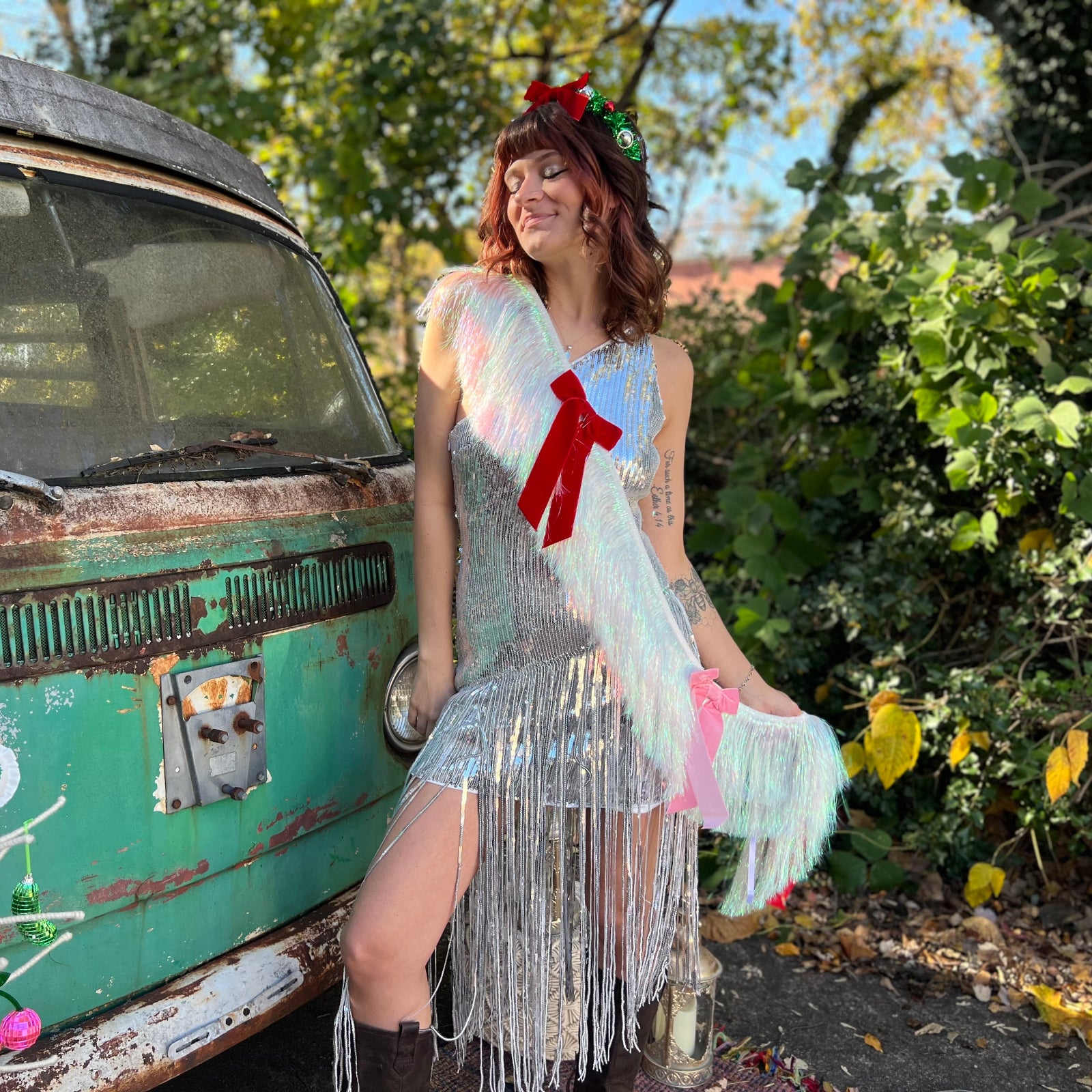 A woman in a silver sequin dress wearing the Bow Bliss Layered Fringe Banner in front of a vintage teal Volkswagen bus.