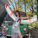 A woman in a silver sequin dress holding the Bow Bliss Layered Fringe Banner in front of a vintage teal Volkswagen bus.