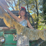 A woman holding the Stay Golden Scalloped Fringe Banner in front of a teal vintage Volkswagen bus.
