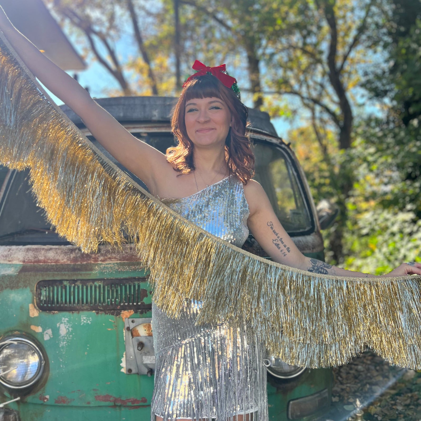 A woman holding the Stay Golden Scalloped Fringe Banner in front of a teal vintage Volkswagen bus.