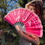 A woman in a silver sequin dress holding the Pink Pony Club Ruffled Folding Fan in front of her face.