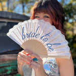 A woman in a silver sequin dress holding a Bride to Be Lace Embroidered Folding Fan.