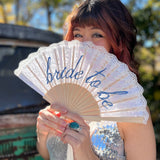 A woman in a silver sequin dress holding a Bride to Be Lace Embroidered Folding Fan.