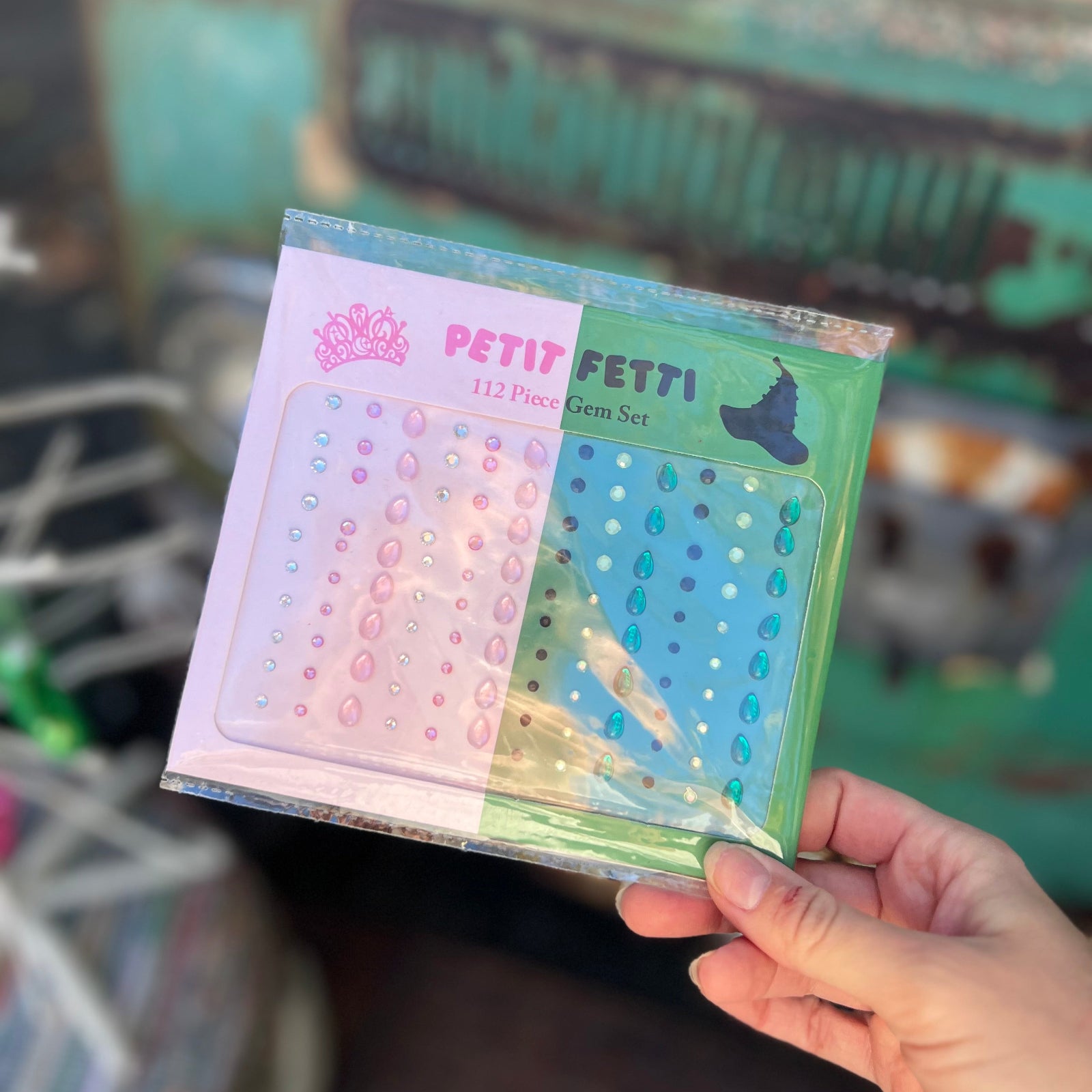 Someone holding the Wicked Inspired Pink Green Face Gem Set in front of a vintage teal Volkswagen bus.