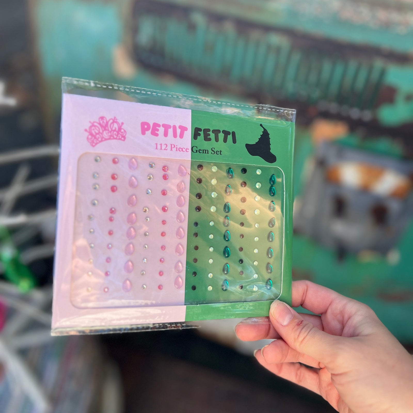 Someone holding the Wicked Inspired Pink Green Face Gem Set in front of a vintage teal Volkswagen bus.