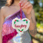 Someone holding the Naughty or Nice Christmas Cross Stitch Double Sided Heart Ornament showing off the naughty side.