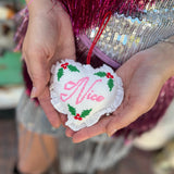 Someone holding the Naughty or Nice Christmas Cross Stitch Double Sided Heart Ornament showing off the nice side.