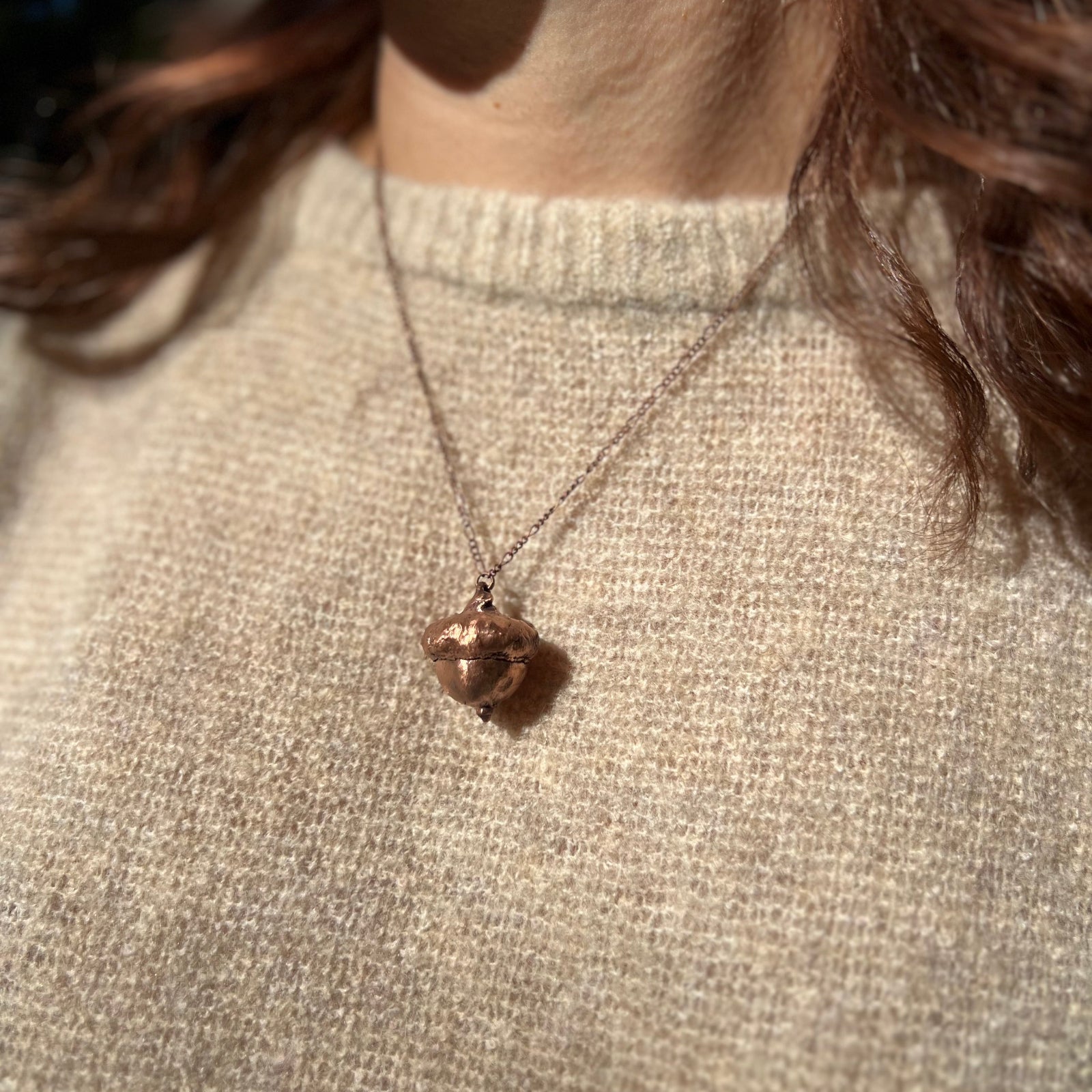 A woman wearing the Real Copper Acorn Necklace with a beige sweater.
