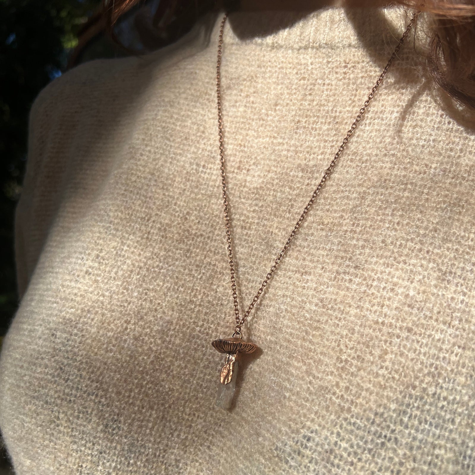 Someone wearing the Kunzite Crystal Copper Mushroom Necklace with a beige sweater.