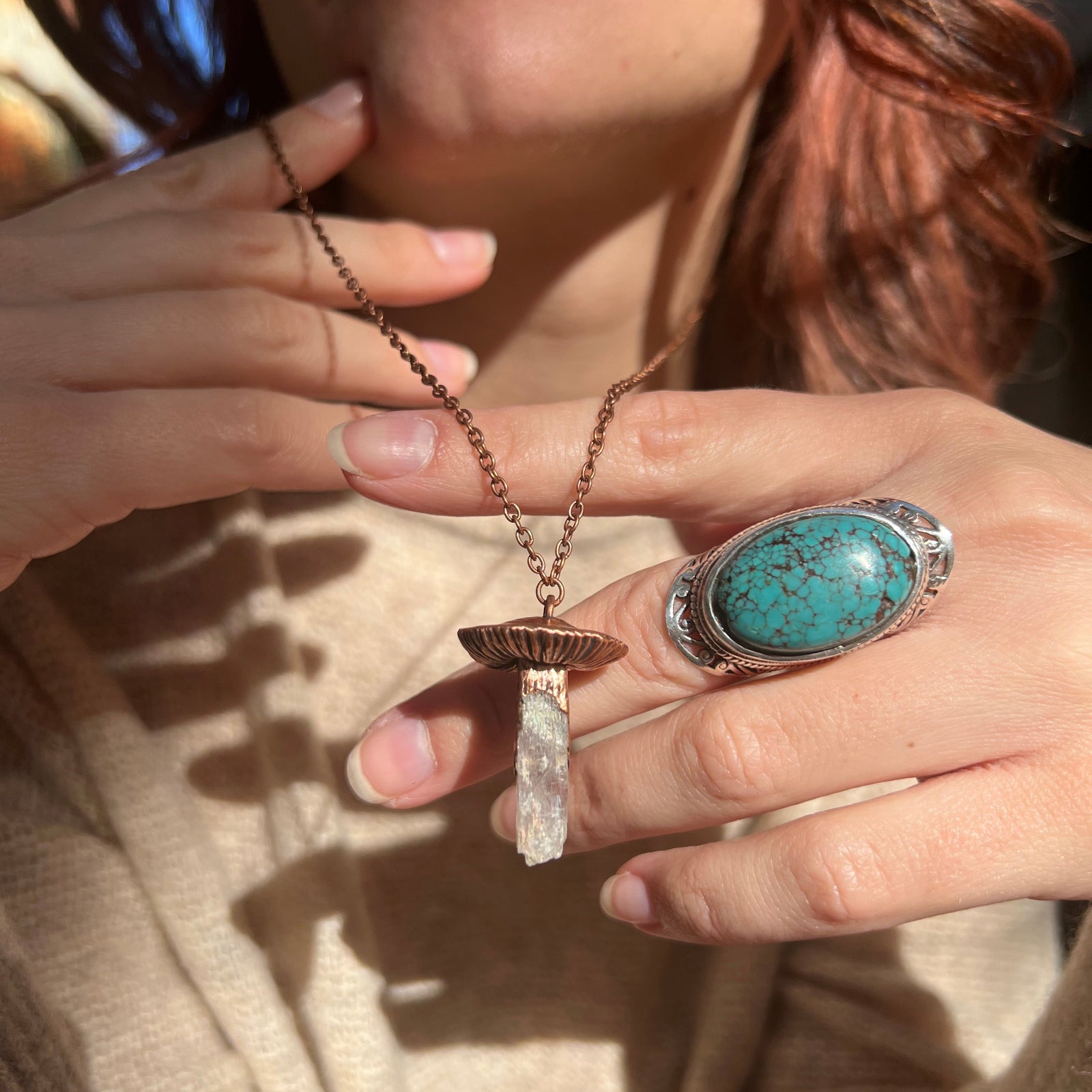 Someone wearing the Kunzite Crystal Copper Mushroom Necklace with a beige sweater.