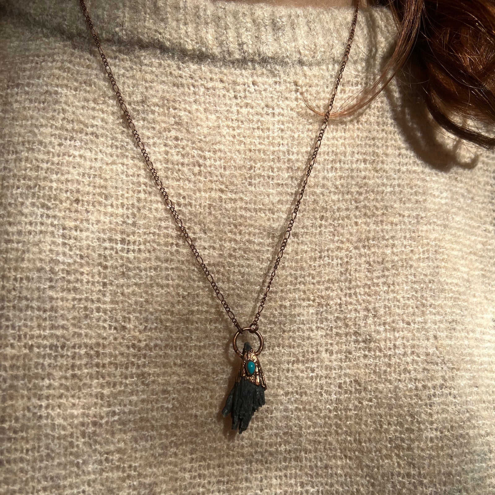 Someone wearing the Black Kyanite Electroformed Necklace with Turquoise and a beige sweater.
