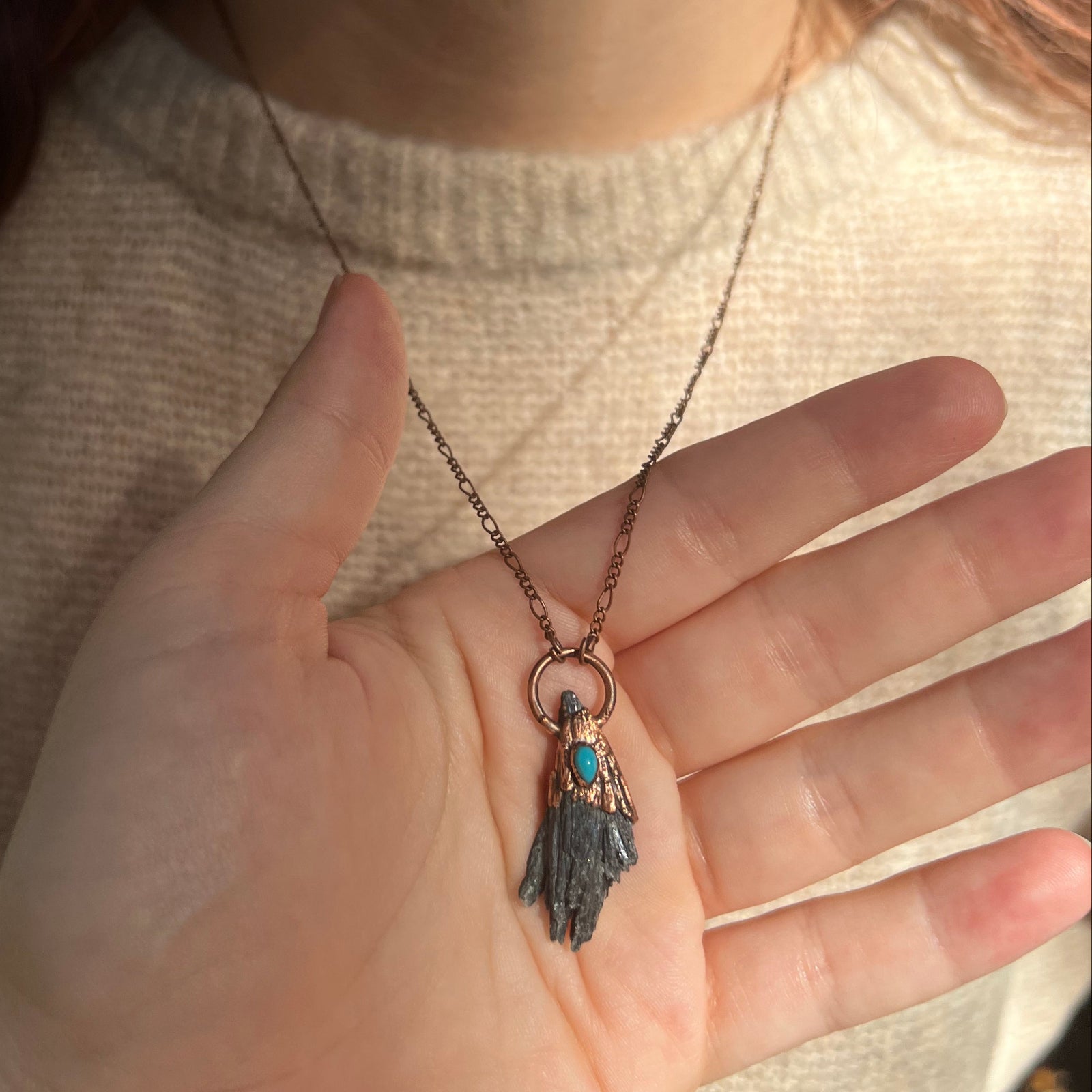 Someone wearing the Black Kyanite Electroformed Necklace with Turquoise and a beige sweater.