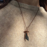 Someone wearing the Black Kyanite Crystal Copper Mushroom Necklace with a beige sweater.