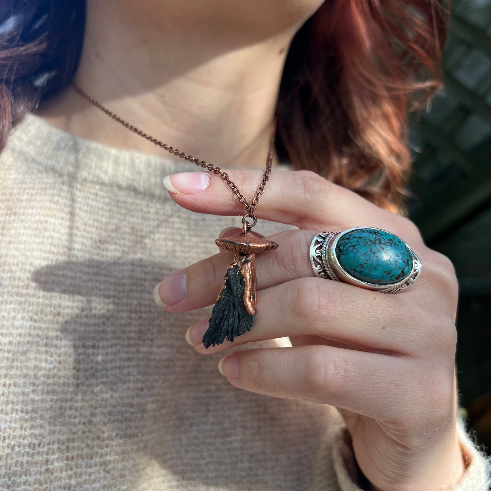 Someone wearing the Black Kyanite Crystal Copper Mushroom Necklace with a beige sweater.