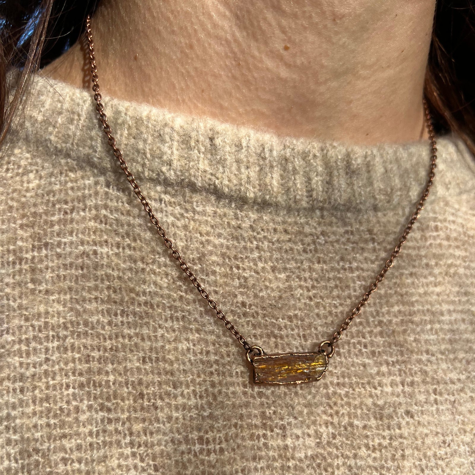 Someone wearing the Orange Kyanite Bar Crystal & Copper Necklace with a beige sweater.