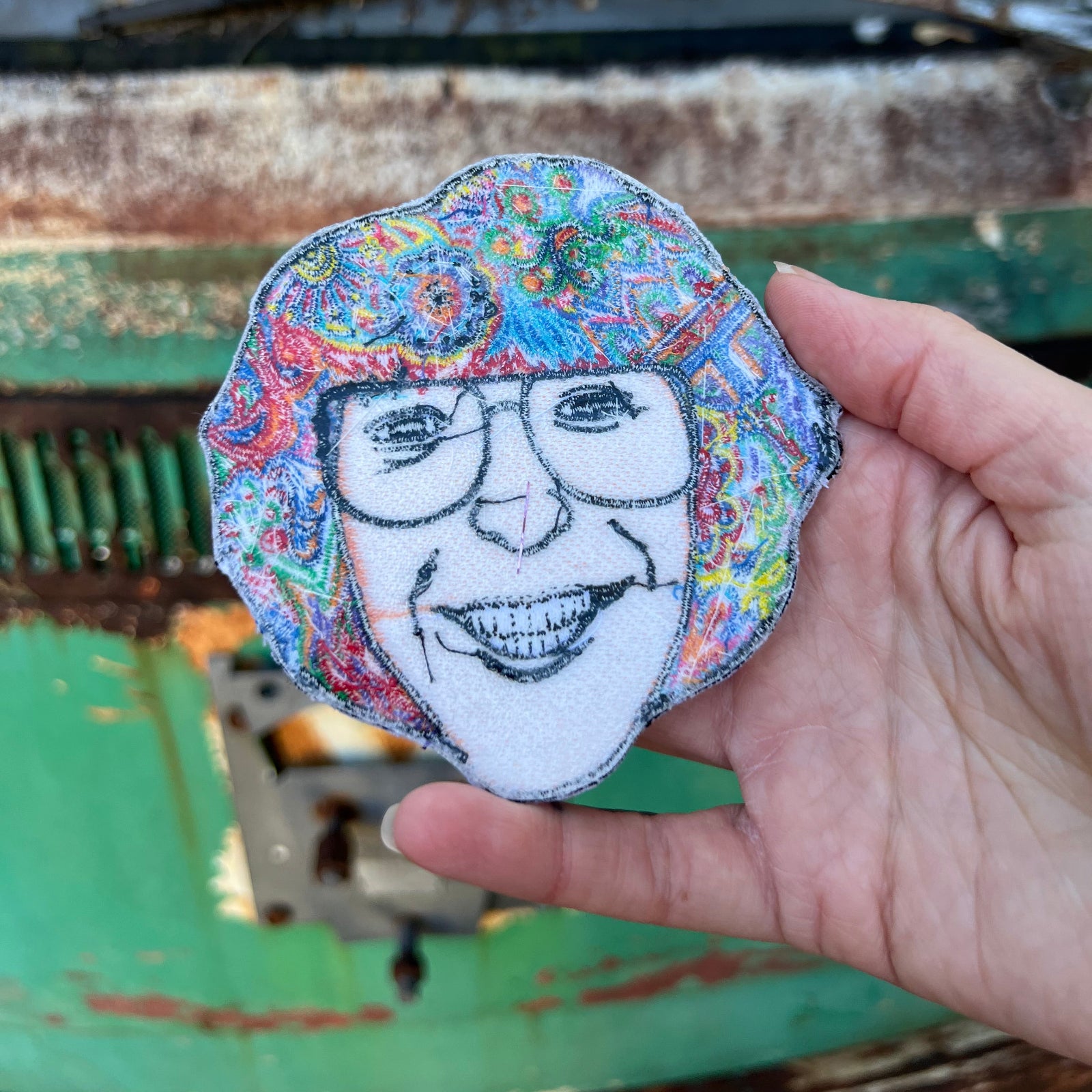 Someone holding the Phil Lesh Grateful Dead Patch in front of a vintage teal Volkswagen bus, showing off the back.