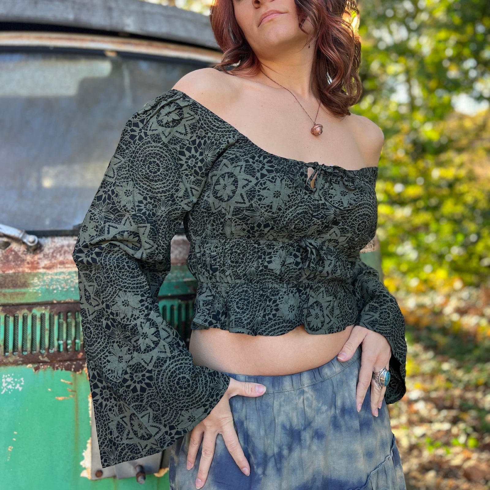 A woman wearing the forest Flowy Peasant Viscose Print Blouse with a skirt in front of the vintage teal Volkswagen bus.